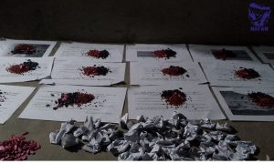 Dark seed and red seed piled on sheets of white paper with wrapped packets below