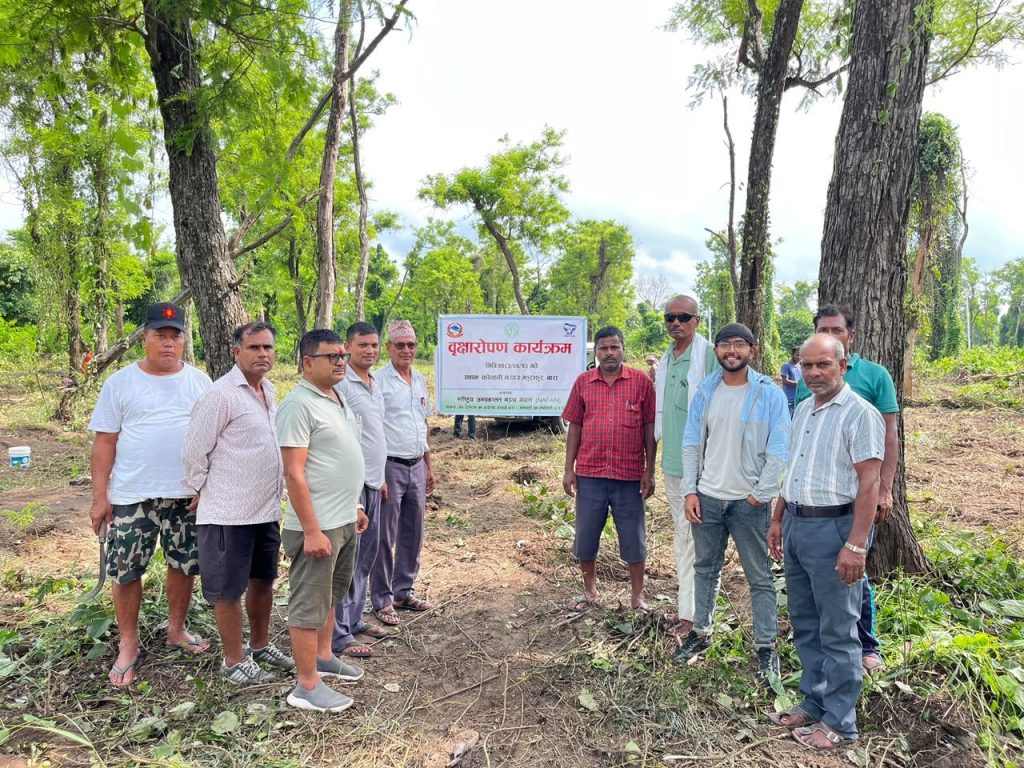 A group of forest users, forest office staff and NAFAN team members standing under a tree plantation programme banner