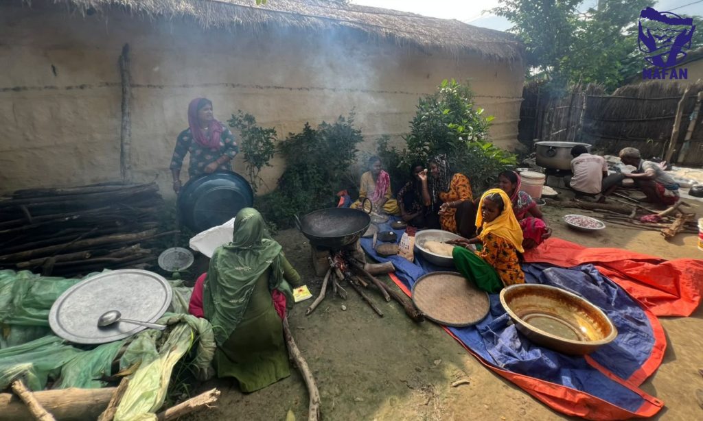 An open-air community kitchen with cooking pots over wood fires and smoke rising