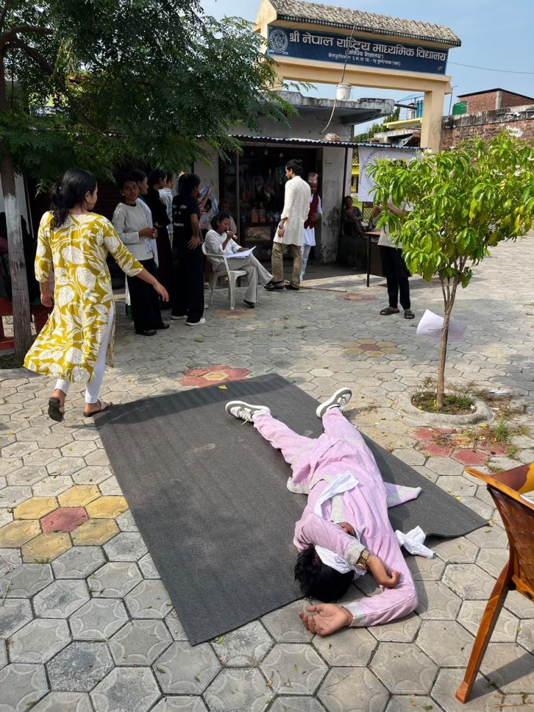 Youth performers act out a scene on a mat in front of a school gate